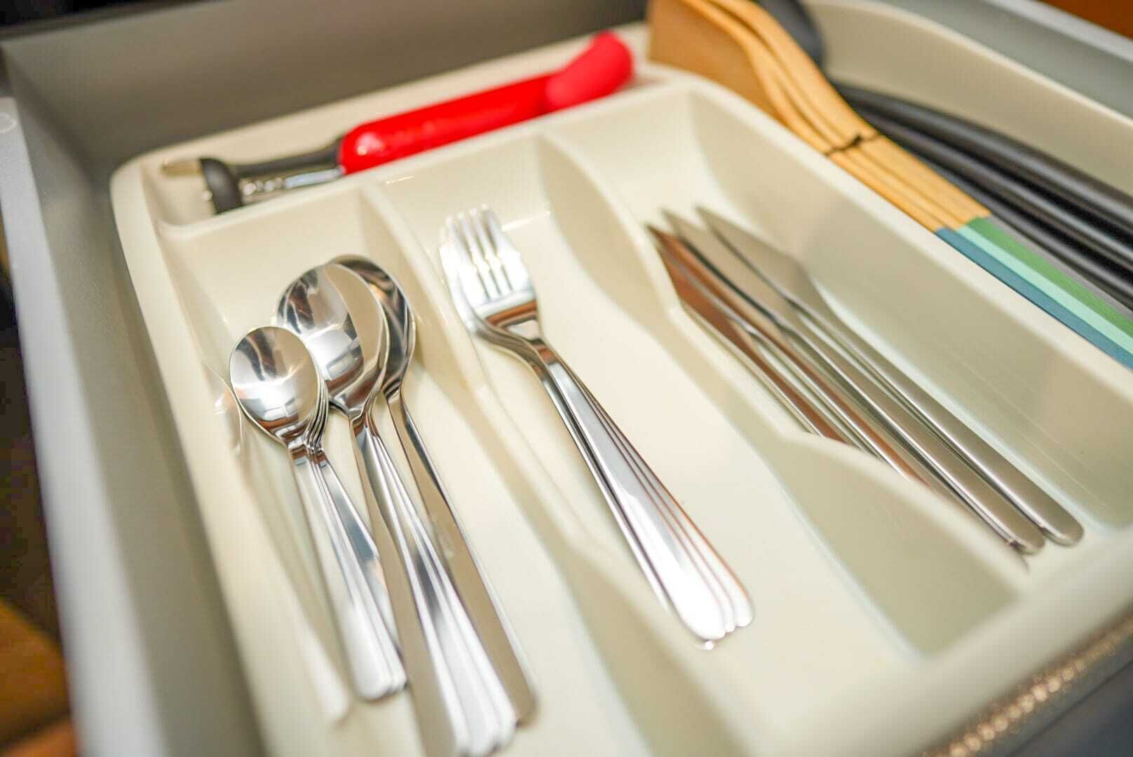 A drawer containing a spoon, fork, and knife with a red handle.