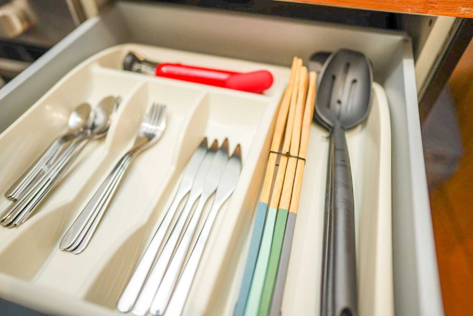 Een lade met verschillende serviezen, waaronder vorken, lepels en stokjes.