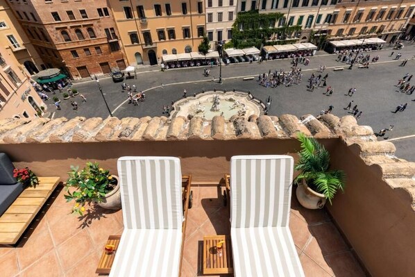 A balcony with two striped lounge chairs, a small table, and potted plants.