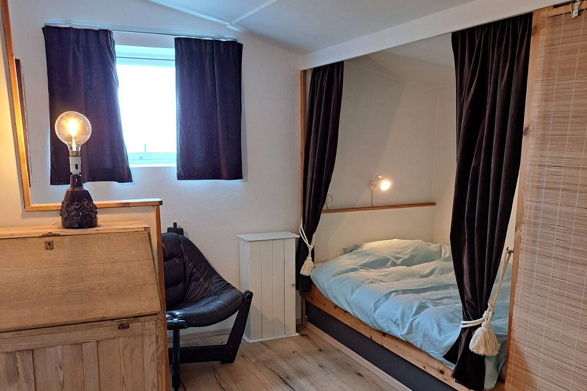 Makuuhuone, jossa on sänky, puinen lipasto, tuoli, yöpöytä ja lamppu.