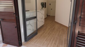 A hotel entrance with a brown doormat, a wooden floor, and a glass door leading to a room with a marble countertop. - Emar Hotel (Tirana)