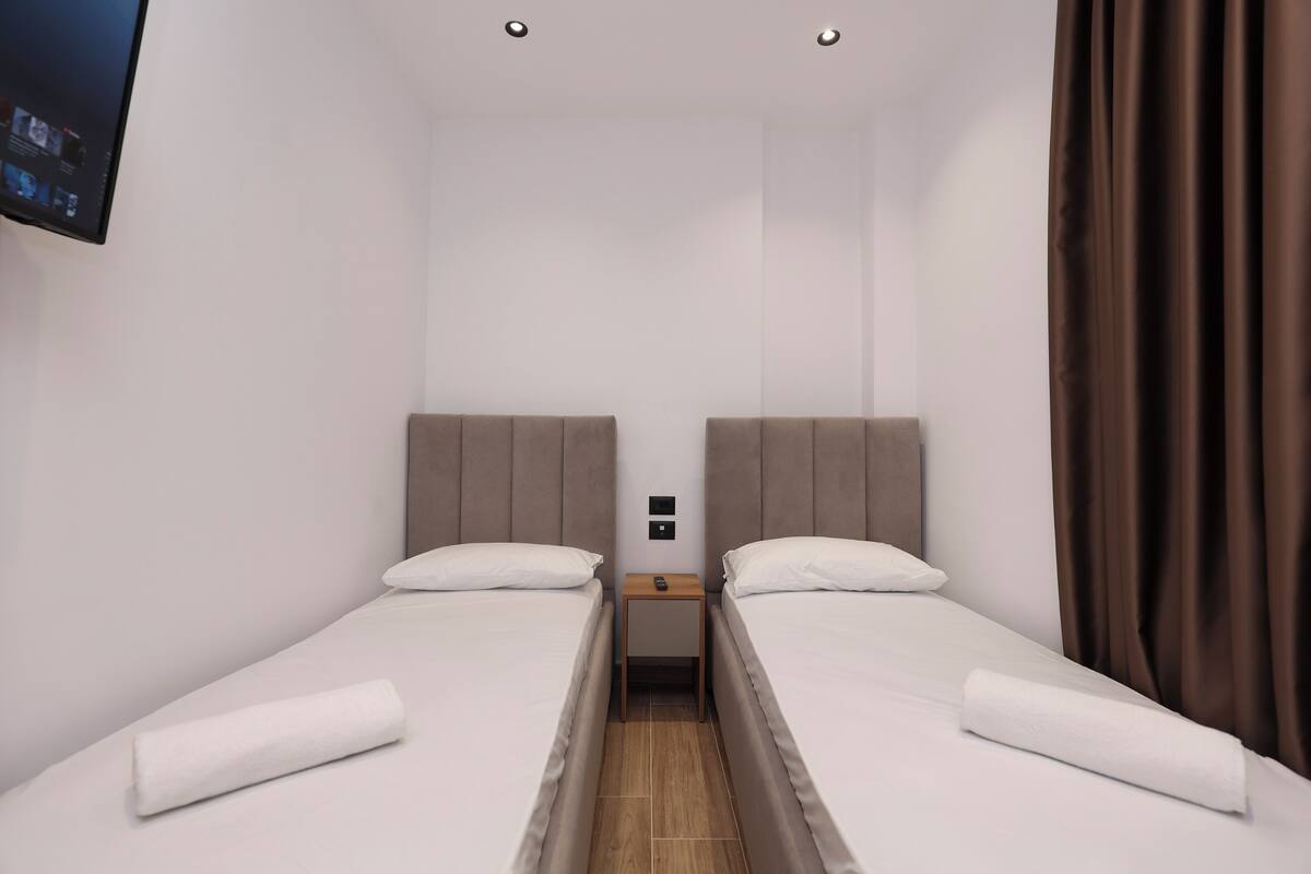 A twin room with two beds, a TV mounted on the wall, and a wooden nightstand between the beds.