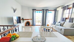 A modern living room with a sofa, TV, fireplace, and a dining area with a table and chairs.