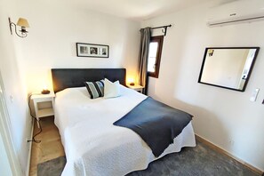 Une chambre à coucher bien rangée, avec un lit, des lampes de chevet, un tableau encadré, un miroir et un appareil de climatisation.