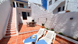 A sunlit patio with white lounge chairs, a table, and a staircase leading to a balcony. - Los Naranjos 15A (Nerja)