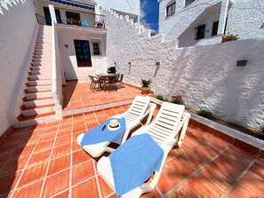 A sunlit patio with white lounge chairs, a table, and a staircase leading to a balcony. - Los Naranjos 15A (Nerja)