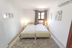 A small, clean room with a single bed, two bedside lamps, a window with curtains, and a wall-mounted air conditioner. - Los Naranjos 15A (Nerja)