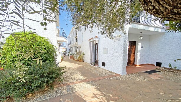 A narrow, paved pathway flanked by white buildings with balconies, leading to a wooden door. - Los Naranjos 15A (Nerja)