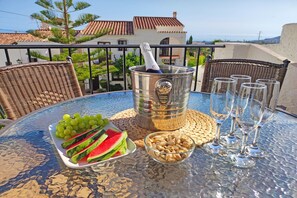 A table with a metal bucket, a bowl of nuts, a plate of watermelon and grapes, and several glasses on a balcony overlooking a coastal area. - Los Naranjos 15A (Nerja)