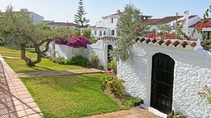 A traditional white-washed building with a tiled roof, a well-maintained garden with grass and flowering plants, and a paved walkway.