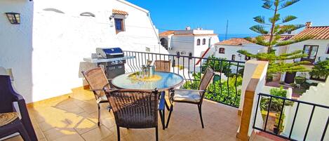 Un balcon avec une table ronde et des chaises, un barbecue et une vue sur le quartier.