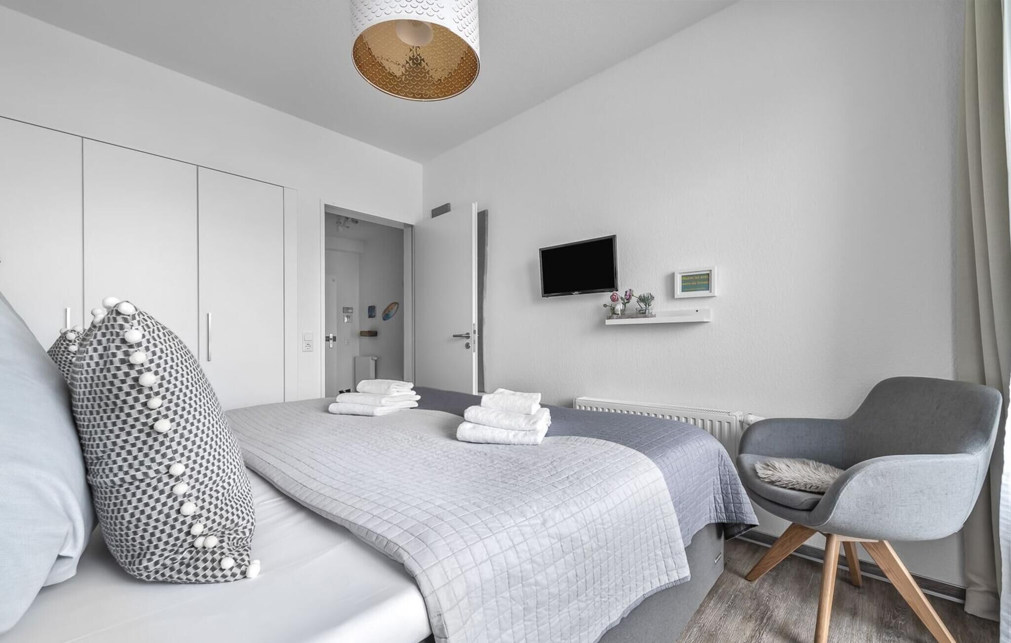 A modern bedroom with a bed, two bedside tables, a chair, a TV, and a shelf with a picture and a plant.