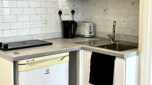 Ett kompakt kök med vita skåp, en inbyggd diskmaskin, en brödrost och ett handfat.