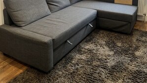 En grå, modulbaserad soffa med en träpanel som accent, en rund spegel på väggen och ett fönster med mönstrade gardiner.