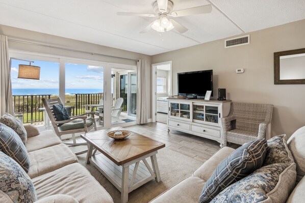 Un salon comprenant un grand canapé, une table basse, un téléviseur et un balcon avec vue sur l’océan.