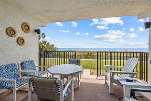 Une terrasse couverte, aménagée avec du mobilier d’extérieur, une table et des tournesols décoratifs accrochés au mur.