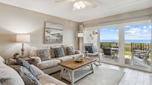 A living room with a sofa, coffee table, and a view of the ocean through large sliding glass doors. - Oceanfront 1st-Floor Oasis: Steps to Pool & Beach (Fernandina Beach)