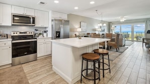 A modern kitchen with white cabinetry, stainless steel appliances, and a central island with stools. - Oceanfront 1st-Floor Oasis: Steps to Pool & Beach (Fernandina Beach)