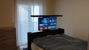 A bedroom with a bed, a TV mounted on a stand, a wooden dresser, and a window with blinds. - Ferienwohnung Direkt am Meer Erste Reihe Insel Vir 25km von Zadar (Vir)