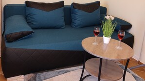 A blue sofa with dark cushions, a small round wooden table with two wine glasses and a potted plant, and a painting of sailboats on the wall. - Ferienwohnung Direkt am Meer Erste Reihe Insel Vir 25km von Zadar (Vir)