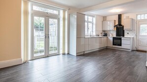 A spacious kitchen with white cabinets, a black range hood, and a large window.