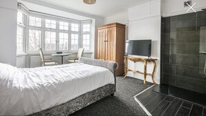 A hotel room with a bed, a TV, a wooden wardrobe, a small table, and a shower area.