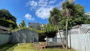 A backyard with a wooden deck, a small shed, and a tall palm tree.