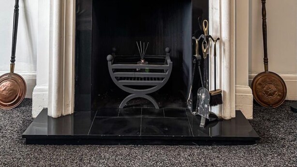 A fireplace with a gold-framed mirror above it, a black mantel, and a modern light fixture.