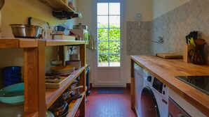 Una cocina compacta con estantes de madera, una lavadora y una ventana con vistas al verdor.