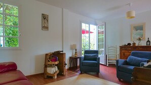 Una sala de estar con un sofá rojo, dos sillones azules, un aparador de madera y una mesita con una lámpara.