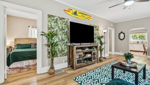 A living room with a television, a bookshelf, a green sofa, and a patterned rug. - NEW-Parrot Head Haven-3BR-1BA-Themed-Bar-Patio (Piqua)