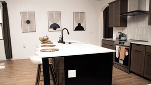 Une cuisine moderne dotée d’un îlot central, de tabourets de bar et d’un four encastré.