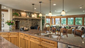 A kitchen with granite countertops, wooden cabinets, a stone fireplace, and pendant lighting. - 🏔️ Four Sisters Mountain Haven: Luxury, Hot Tub, Near Ski Lift & Village, $0 Cleaning & Pet Fee (Keystone)