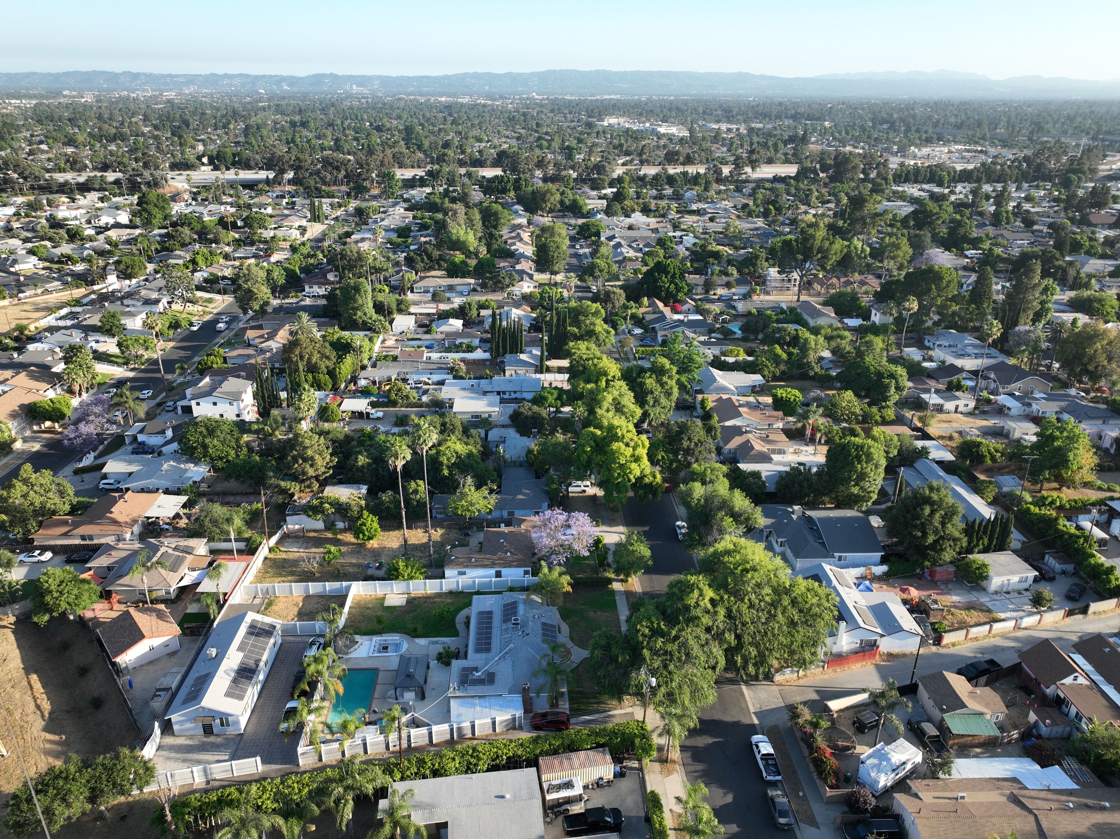 An aerial view of a residential area with houses, a swimming pool, and a large building with solar panels.
