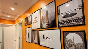 Ein Korridor mit gerahmten Bildern an der Wand, darunter eine Stadtansicht, eine Tastatur und ein Zitat mit der Aufschrift 'love. (is all you need.)'.