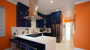 Eine moderne Küche mit dunkelblauen Schränken, einer weißen Kochinsel mit Barhocker, Edelstahlgeräten und einer leuchtend orangefarbenen Akzentwand.