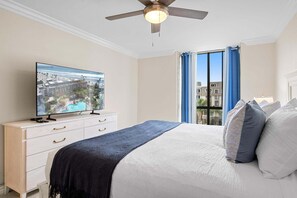 A bedroom with a bed, a TV on a dresser, a ceiling fan, and a window with curtains.