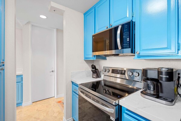 Una cocina con armarios azules, microondas, horno y cafetera Keurig.
