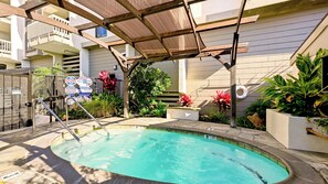 A swimming pool with a metal ladder, surrounded by plants and a covered area.