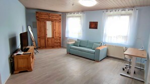 Ein Zimmer mit einem hellblauen Sofa, einem Holzschrank, einem Schreibtisch mit Stuhl und einer Heizung.