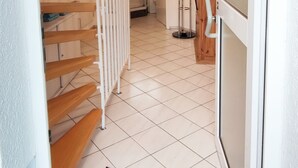 Ein Flur mit einer Holztreppe, einer Glastür und einem gefliesten Boden.