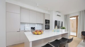 A modern kitchen with white cabinetry, a central island with bar stools, a flat-screen TV, and a built-in oven. - Spacious Apartment | 3 Bedrooms | Parking (Warszawa)