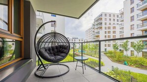 A balcony with a black hanging chair, a small round table, and a view of a residential area with modern buildings. - Spacious Apartment | 3 Bedrooms | Parking (Warszawa)