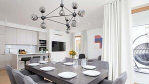 A modern kitchen with white cabinets, a central island, and a dining area with a dark wooden table set for six. - Spacious Apartment | 3 Bedrooms | Parking (Warszawa)