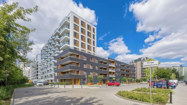 A modern apartment building with multiple balconies, a parking area, and a sign indicating a nearby drug store. - Spacious Apartment | 3 Bedrooms | Parking (Warszawa)