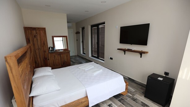 Ein Schlafzimmer mit einem hölzernen Bett, einem an der Wand montierten Fernseher und einer kleinen, schwarzen Kommode.