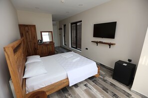 Une chambre avec un lit en bois, un téléviseur fixé au mur et une petite armoire noire.