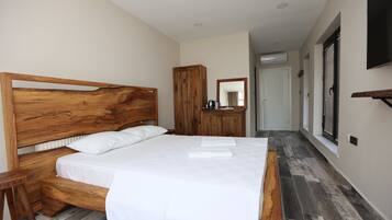 Un dormitorio con cabecera de madera, cama con ropa de cama blanca, armario de madera, espejo y televisión en la pared.