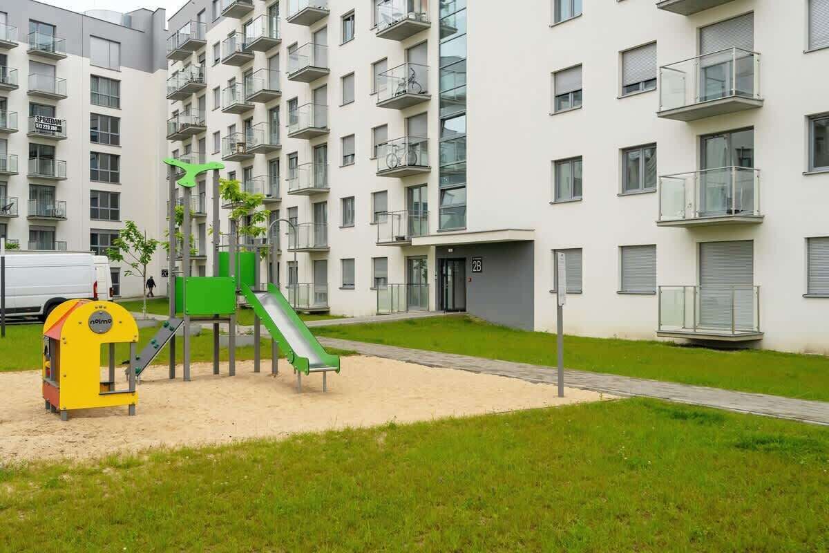 Un terrain de jeux équipé d’un toboggan et de structures d’escalade, entouré d’un immeuble d’habitation doté de balcons et de fenêtres.