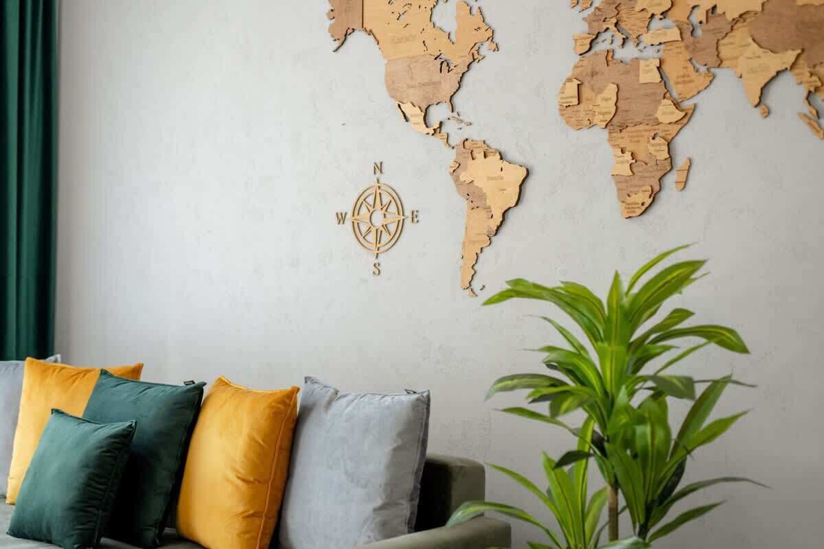A world map wall decoration with a compass rose, a grey sofa with colorful cushions, and a green plant.